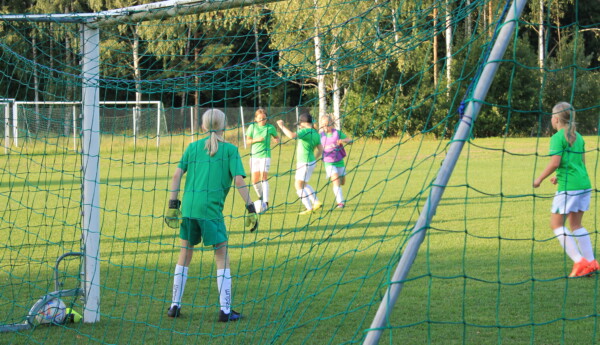 EIF:s fotbollslag med flickor födda 2012 och 2013 håller en träning på en gräsplan i Ekenäs. Bilden är fotograferad bakommålet så man ser målvaktens rygg och några spelare som försöker ta bollen.