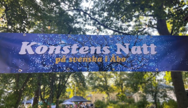 En blå banderoll där det står "konstens natt", parkmiljö i bakgrunden.