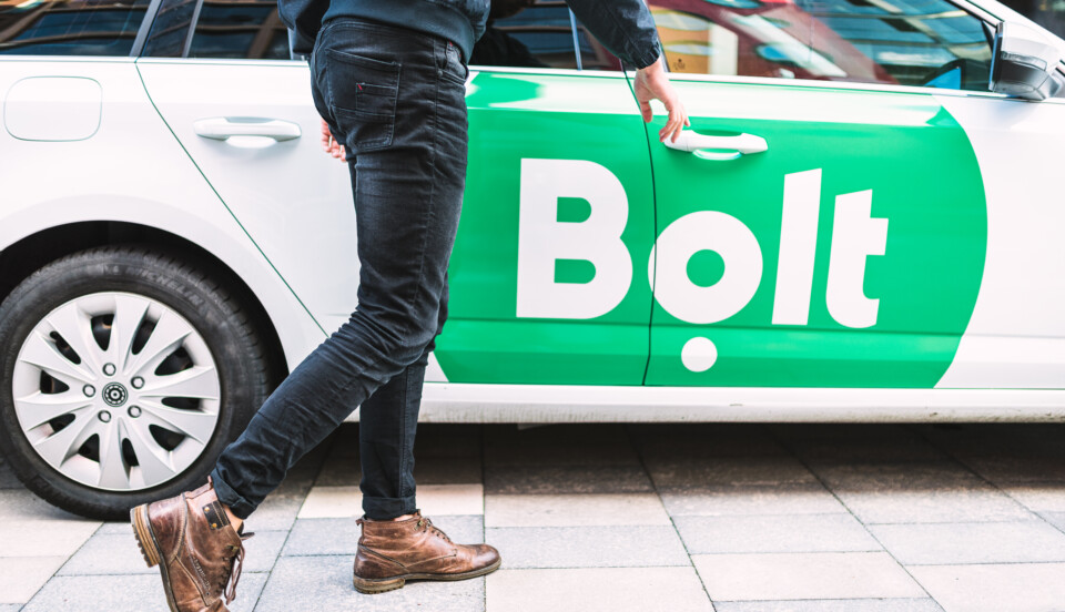 Vit personbil med grön logotyp med texten "Bolt". I förgrunden en person som är på väg att öppna dörren till passagerarsätet