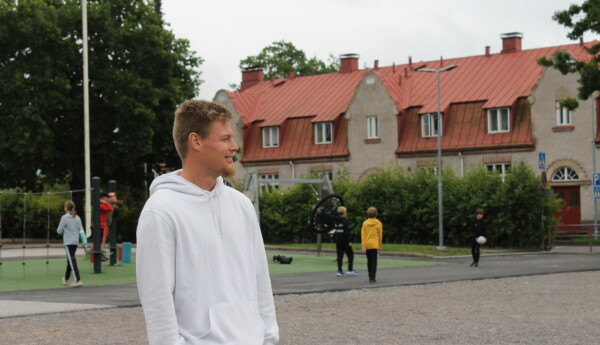En ung man står och tittar ut över Seminarieskolans skolgård i Ekenäs. I bakgrunden ser man barn som leker på gården.