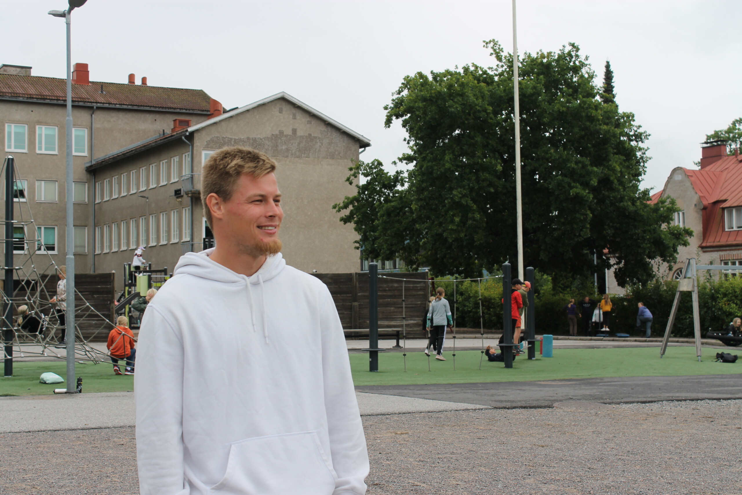 En ung man klädd i vitt står och blickar ut över Seminarieskolans skolgård i Ekenäs. I bakgrunden syns elever som leker.