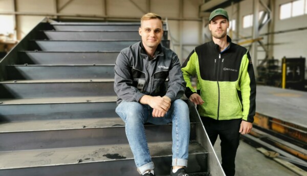 Tvä män i verkstadshall och den ena mannen sitter på en svetsad trappa.