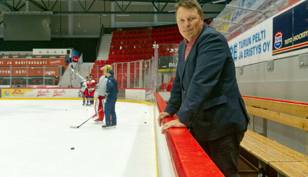 en man i kavaj står vid en hockeyrink