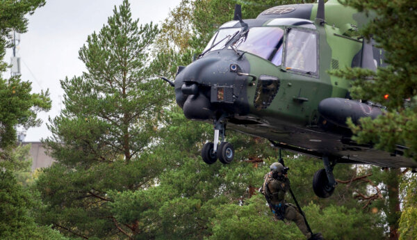 Kamouflagefärgas helikopter sänker ner man i skogen.