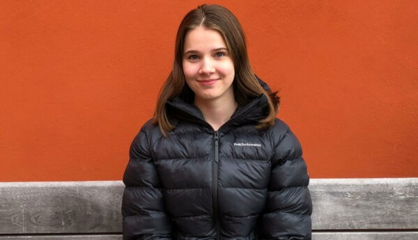 Ung tjej i svart täckjacka framför en rödbrun vägg