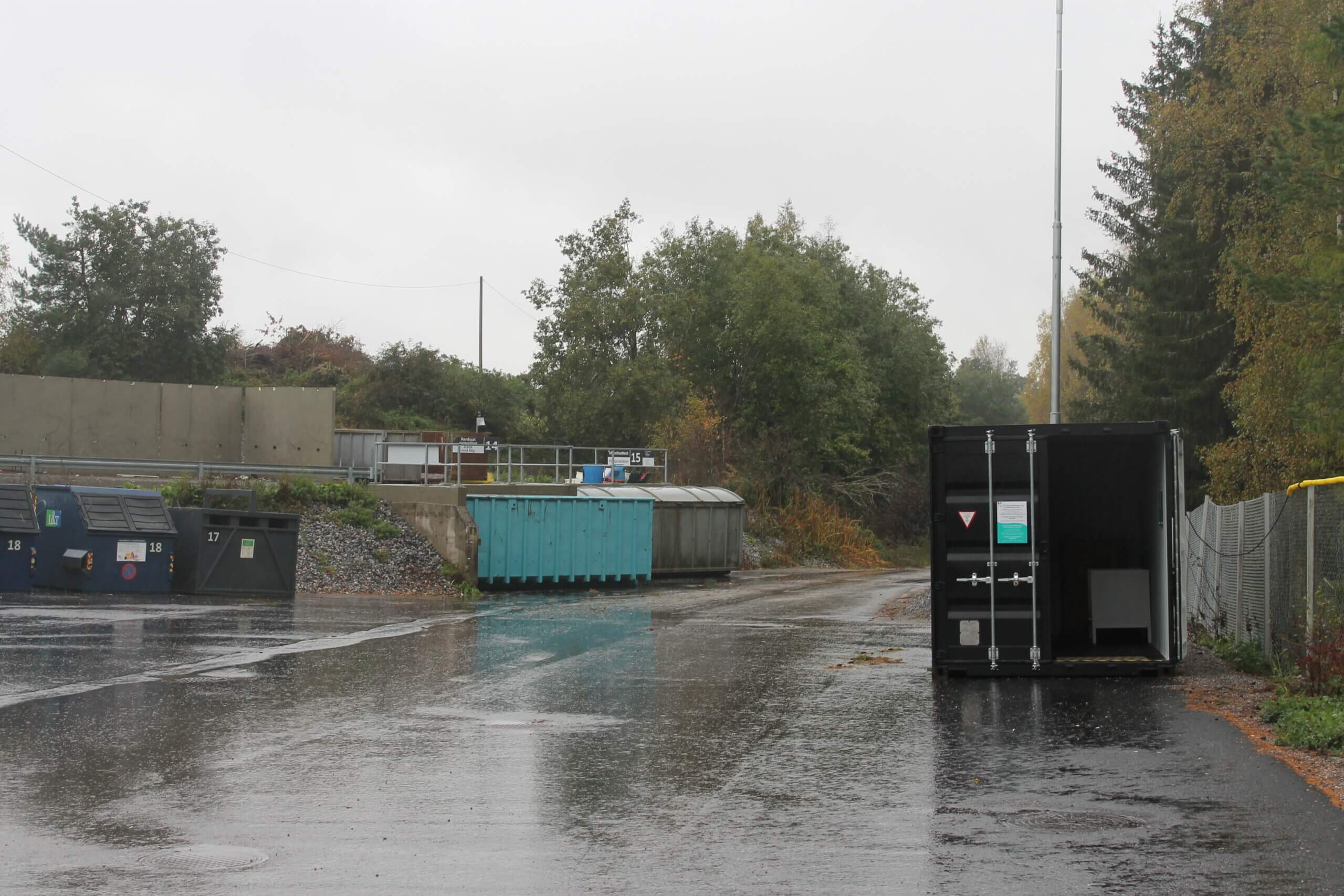 En mulen dag på Karis avfallsstation. En container står vid sidan av ett stängsel och flera containrar syns i bakgrunden.