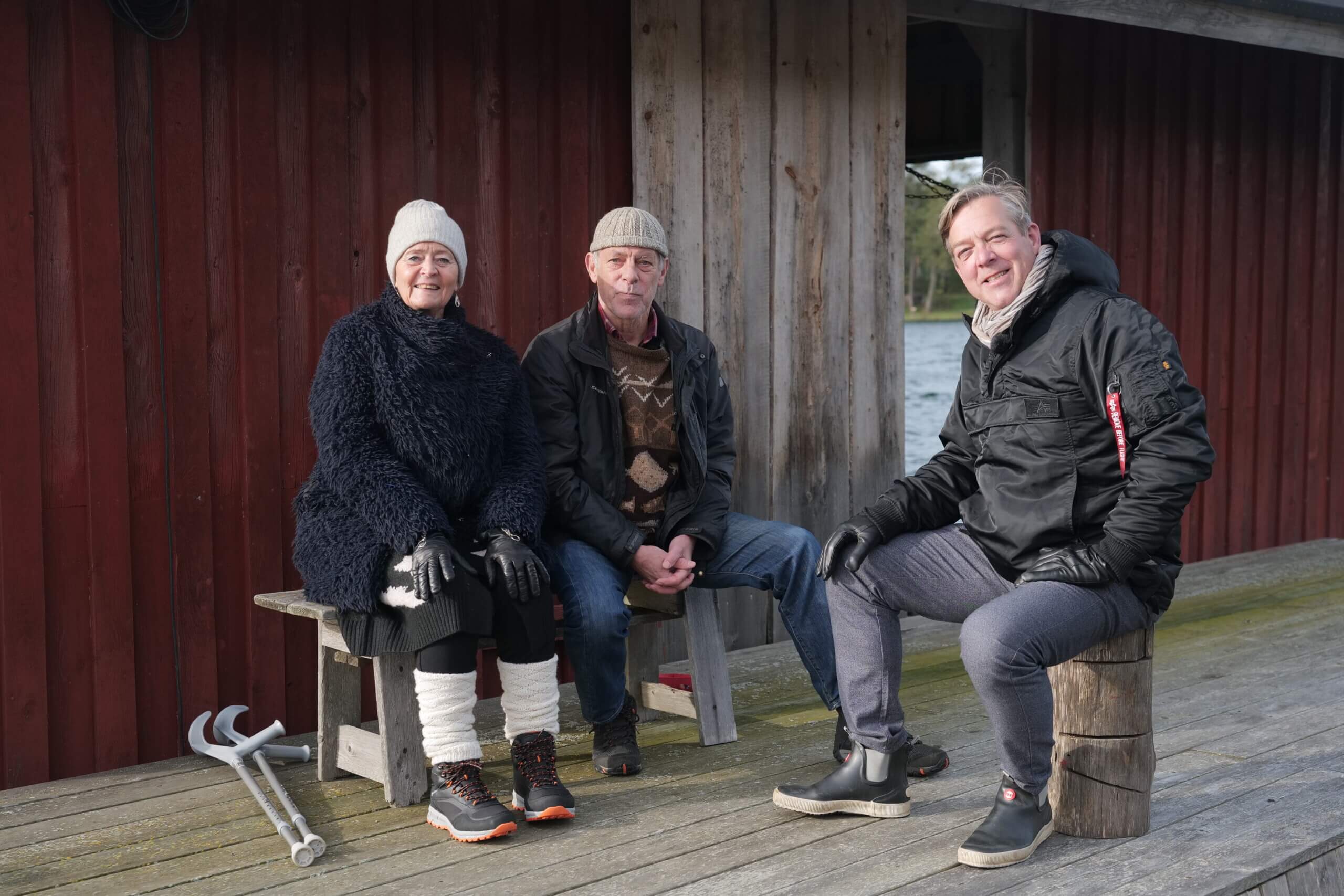 tre personer med vinterkläder sitter på en brygga