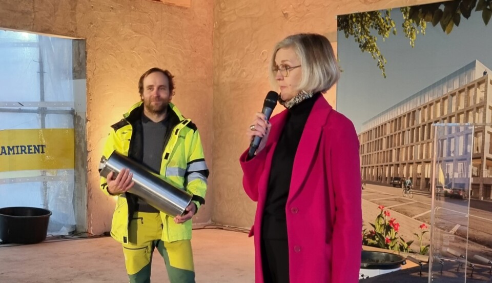 man i varseljacka håller upp stor metallkapsel, kvinna i rosa kappa i förgrunden