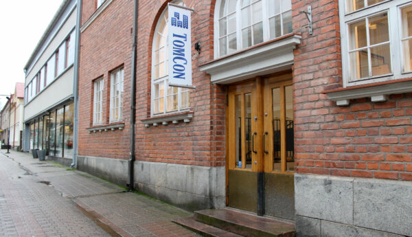Bild på en tegelbyggnad som finns längs Kungsgatan i Ekenäs. Vid byggnadnes dörr hänger en flagga med texten TomCon. Som är ett fastighetsföretag som håller till i byggnaden.