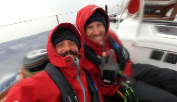 Två seglare ler mot kameran i hård sjögång