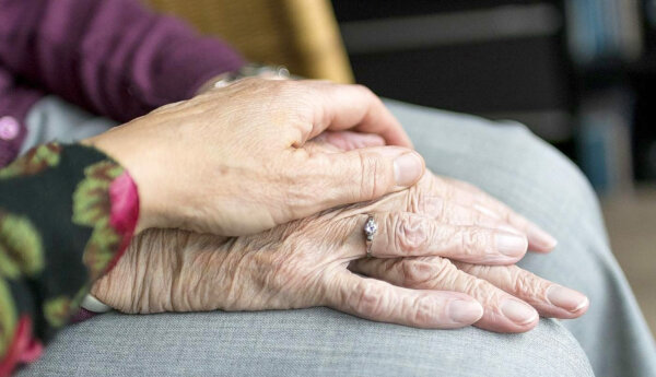 Händer som håller om varandra. Två av de trä händerna tillhör en äldre person.