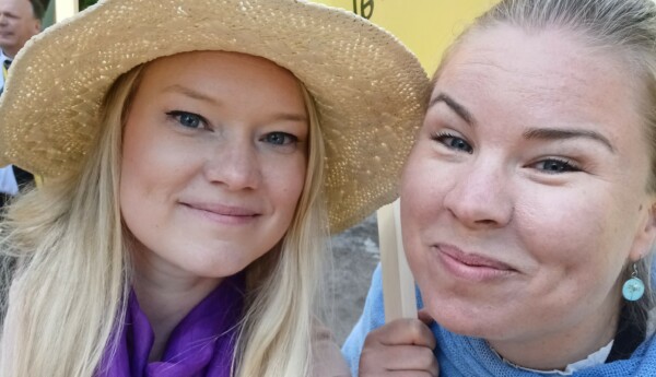 Två blonda leende kvinnor, den ena med hatt.