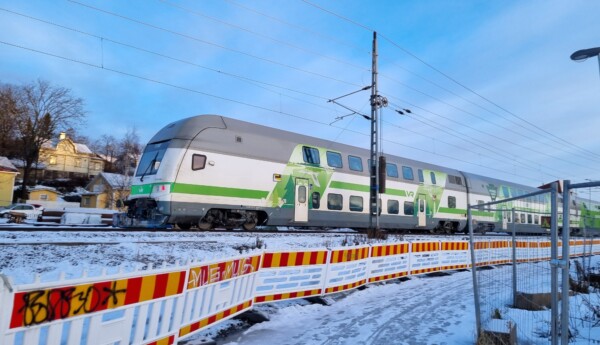 grönvitt tåg passerar, rödgula varselstängsel i förgrunden