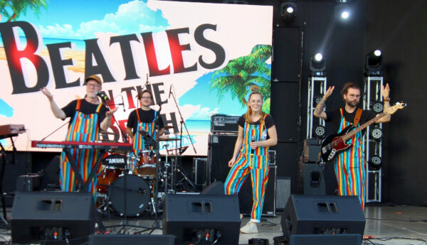 fyra musiker i regnbågsfärgade overaller på en scen med en beatles-logga i bakgrunden