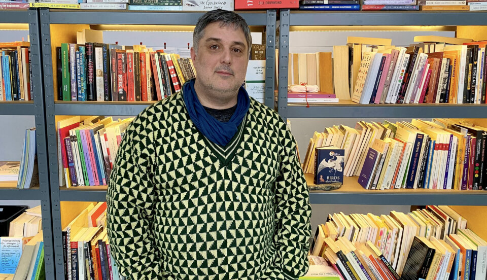 Man i grällt färgad tröja framför en stor bokhylla