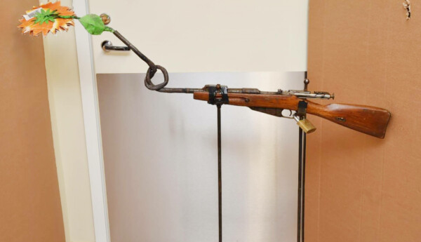 Skulptur bestående av ett gevär med vriden pipa, varifrån det sticker ut en blomma