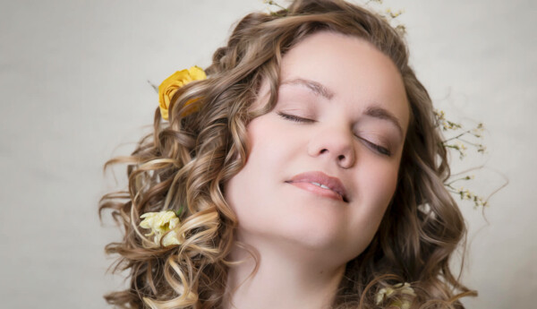 Kvinna med vågigt hår, med blommor i, blundar och lutar sig bakåt