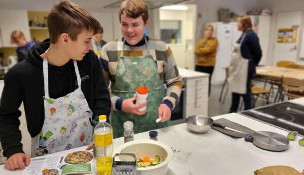 Två pojkar lagar mat i skolkök.