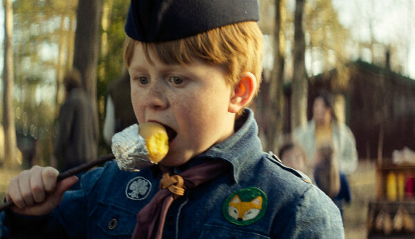 en pojke i scoutuniform äter en grillad potatis