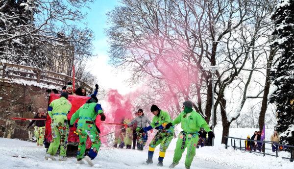Studerande i gröna overaller drar en stor pulka i snöig backe medan röd rök sprutas ut