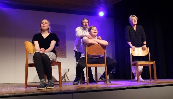 Fyra skådespelare på en scen i Prästkulla revy "Skrattretande". Två av skådespelarna sitter på stolar vända mot publiken och två skådespelare står vända mot publiken.