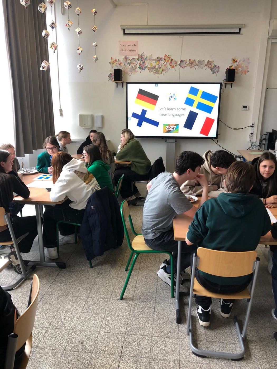 studerande i klassrumsmiljö med flaggor från Tyskland, Sverige, Finland och Frankrike på en skärm