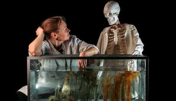 en kvinna sitter vid ett akvarium med ett skelett bredvid sig