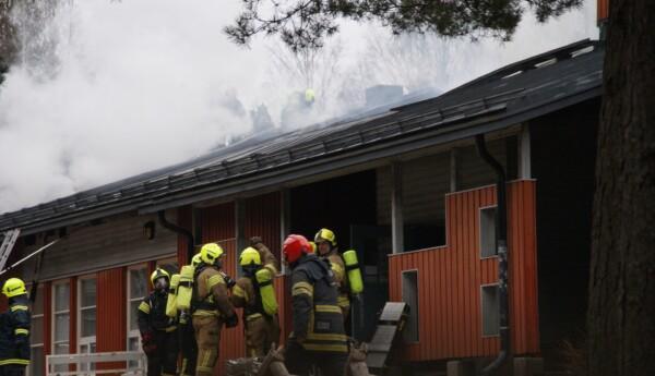 En grupp brandmän framför ett hus med kraftig rökbildning