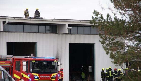 Brandbil vid idustrihall och brandmän på taket.