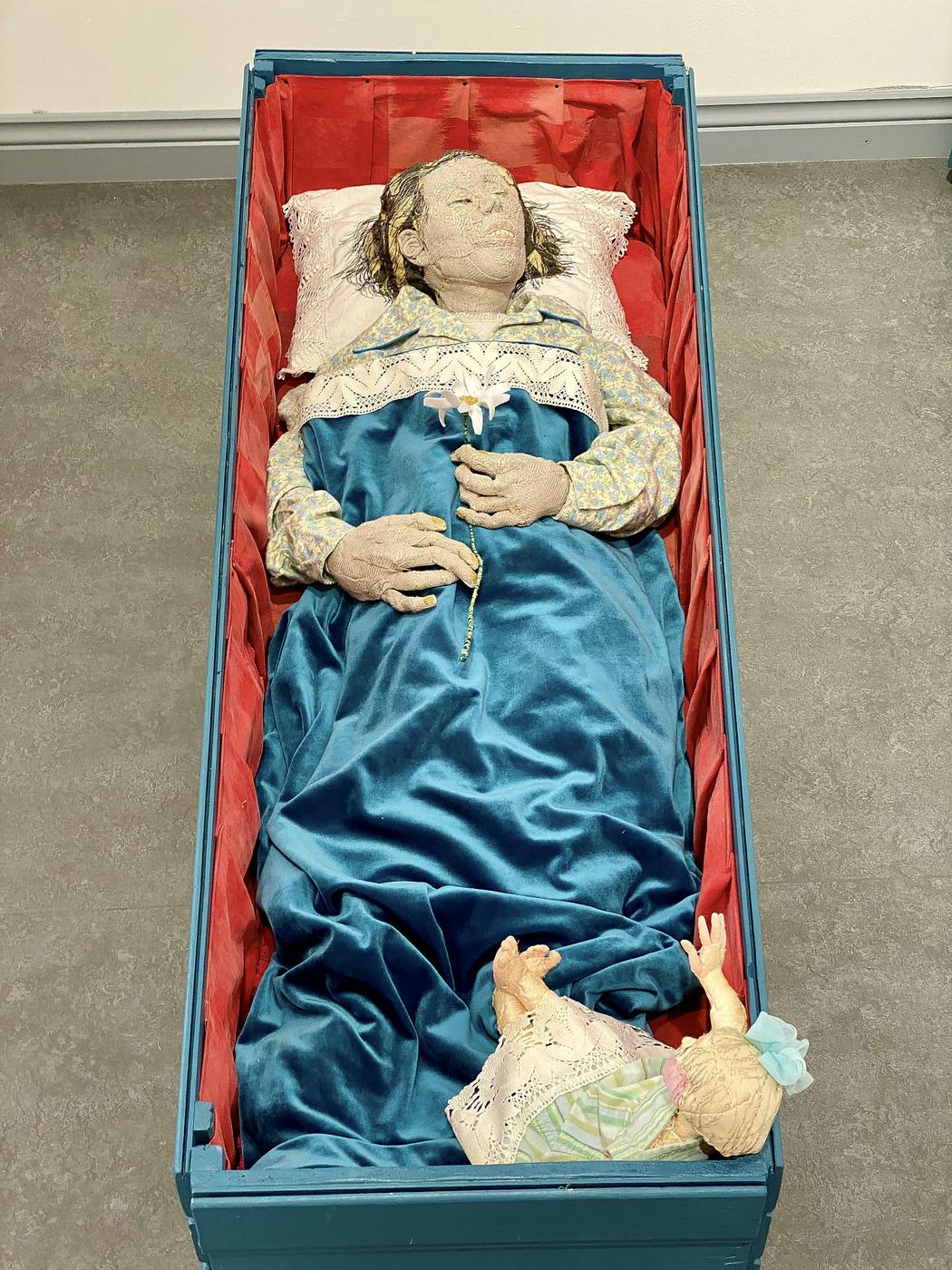 Skulptur som föreställer en människa nedbäddad i en smal kista