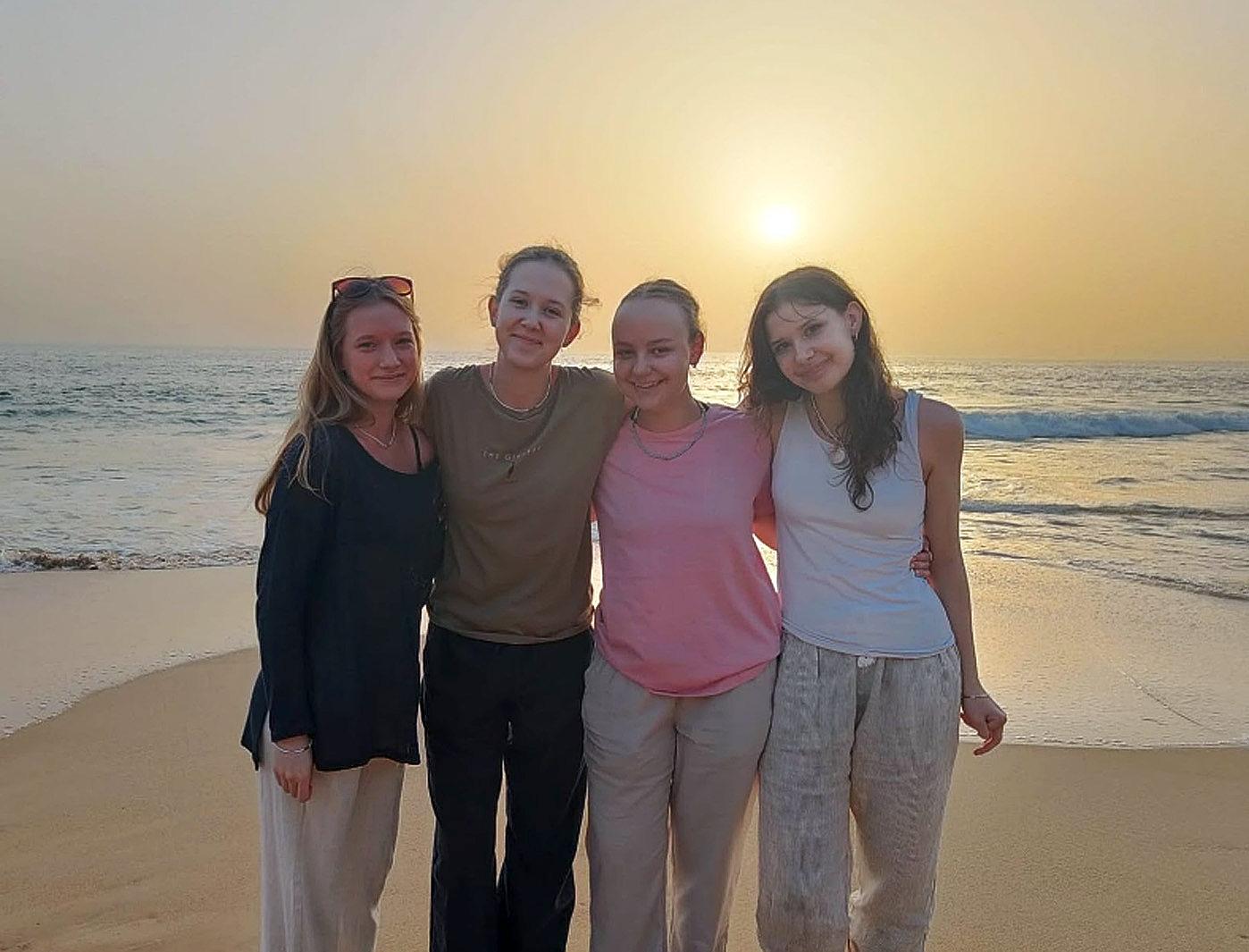 fyra unga kvinnor på en strand, fotade mot en solnedgång