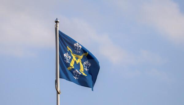 En mörkblå flagga, med stadsvapen i gult och vitt, vajar i flaggstång
