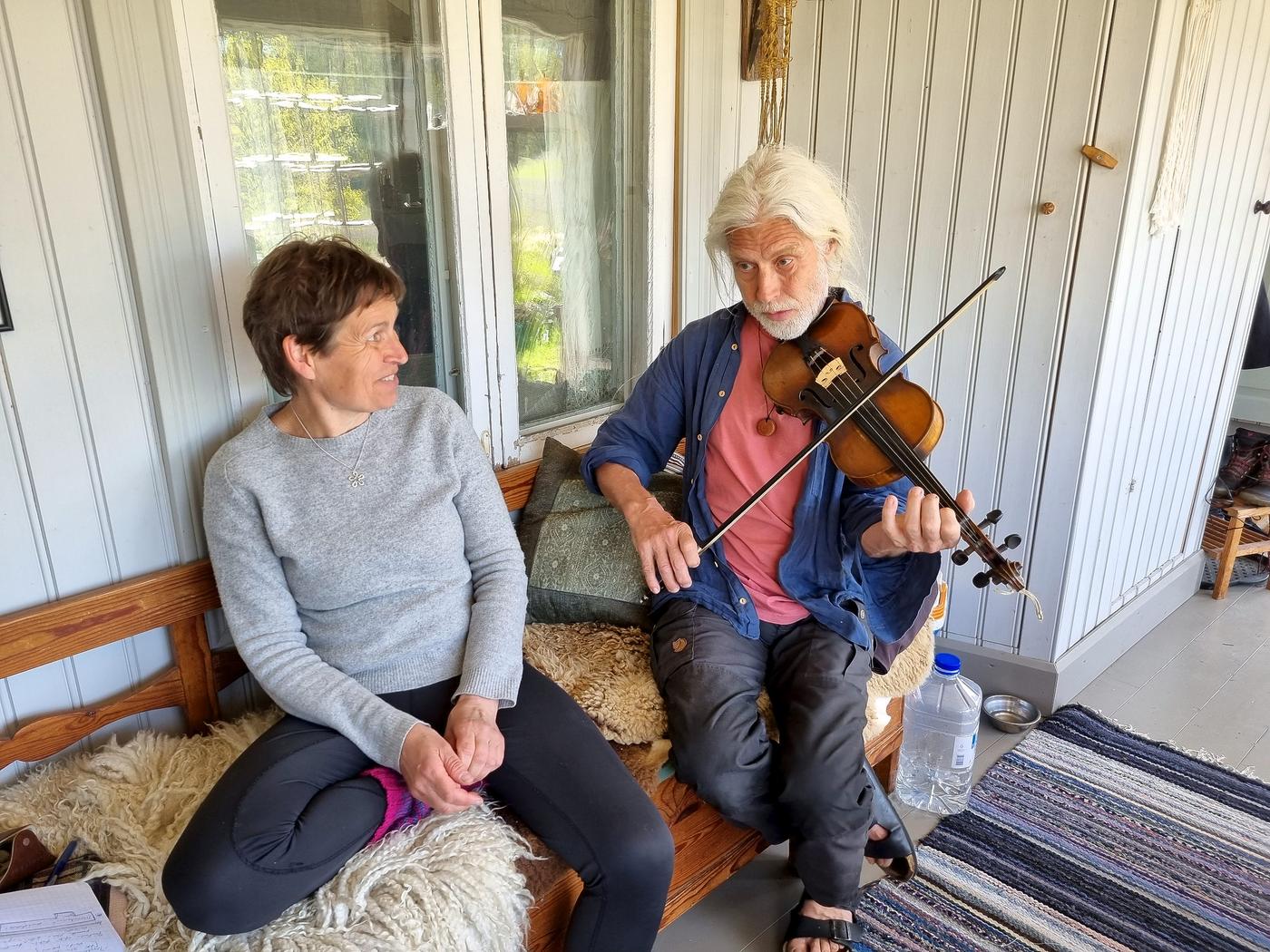 par som sitter på en soffa i ett gammalt hus. mannen spelar fiol.