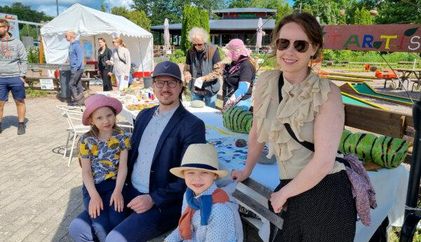 En familj med två barn och två vuxna sitter framför pysselbord på en marknad på sommaren.