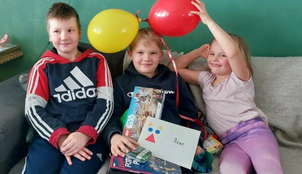 Tre barn i en soffa med ballonger.