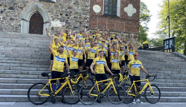 Bild på teamet från åbo framför domkyrkan före start. Alla har gula lagskjortor och cyklar.