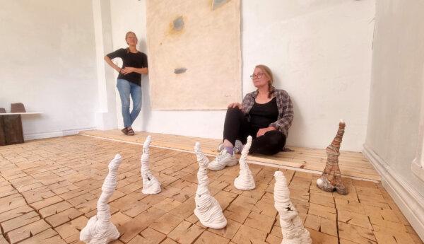 Små skulpturer på ett golv, i bakgrunden två människor varav en sitter och en står