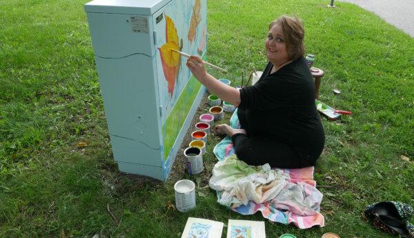 Bild på en glad Helena Mikkola där hon sitter och målar elskåpet med sina målarfärger bredvid sig.