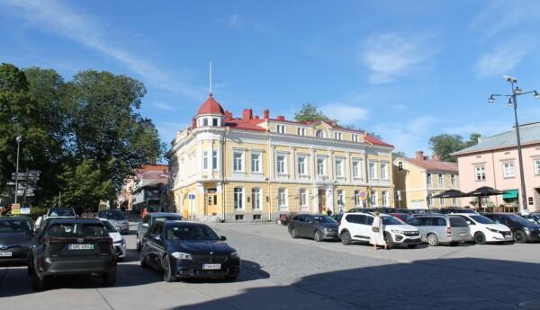Bilar parkerade på Råhustorget i Ekenäs. I bakgrunden ser man ett gult stenhus och en gågata.