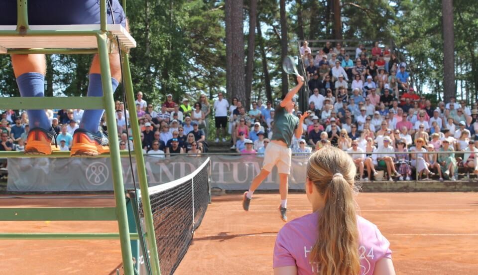 Harri Heliövaara, spelar tennis i Hangö. Närmast kameran är en bollflicka och domarstolen.