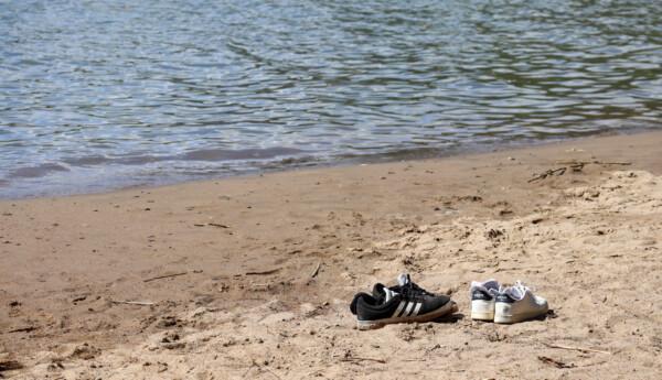 Två par skor på en sandstrand i närheten av vattnet