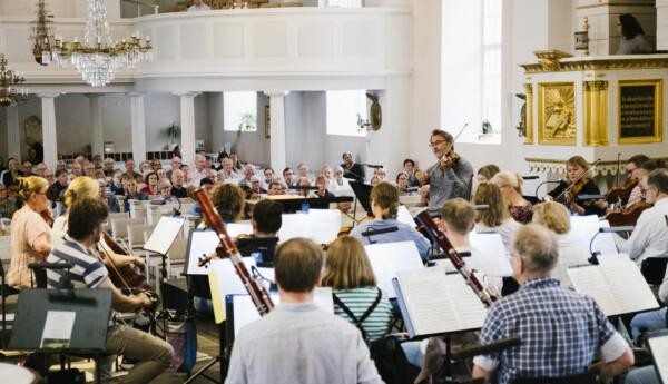 En orkester spelar inför publik i en vit och ljus Ekenäs kyrka.