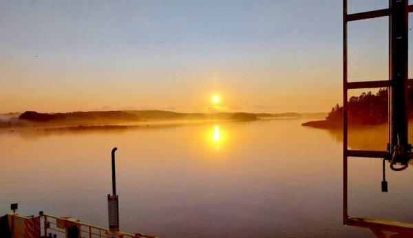 Solen går ner med en färja i förgrunden.