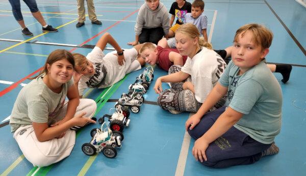 Sju varn sitter på golvet i gymnastiksal och visar upp delego robotar de har byggt.