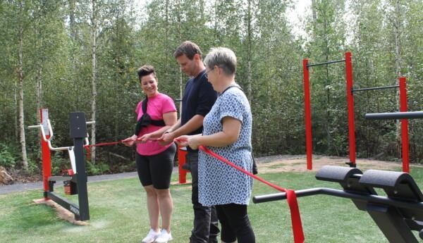 Två kvinnor håller upp ett rött snöre som en man klipper av. Mannen och de två kvinnorna står i Tenalas nya utomhusgym som invigs.