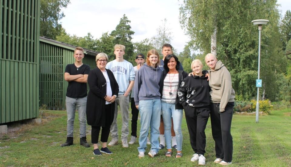 En grupp unga studerande vid Axxell står utomhus på en gräsmatta tillsammans med Axxells enhetschef Beatrice Westerlund och internathandledaren Bettina Lindholm.